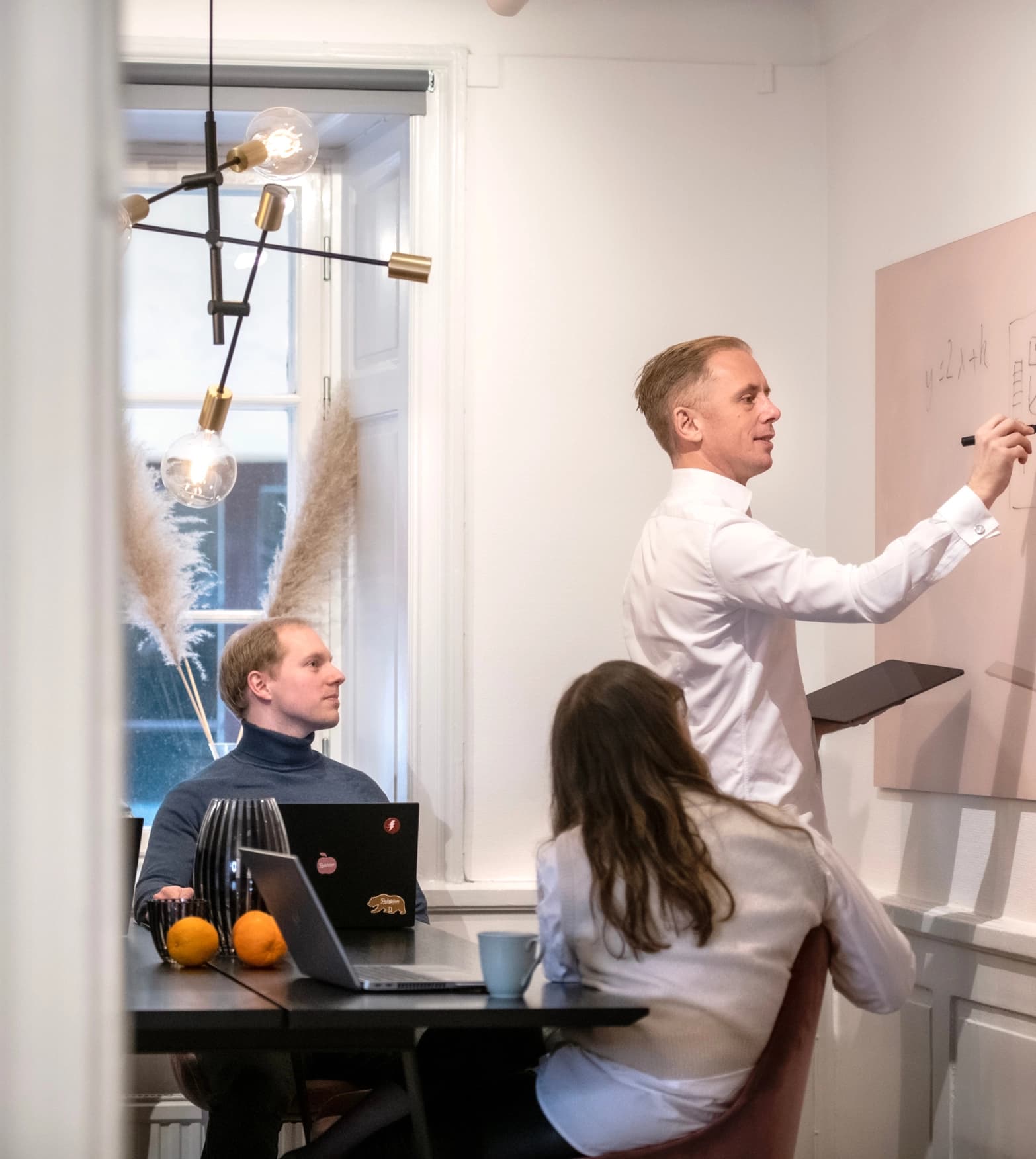 Måns ritar på en whiteboard under ett möte där två andra sitter och tittar på